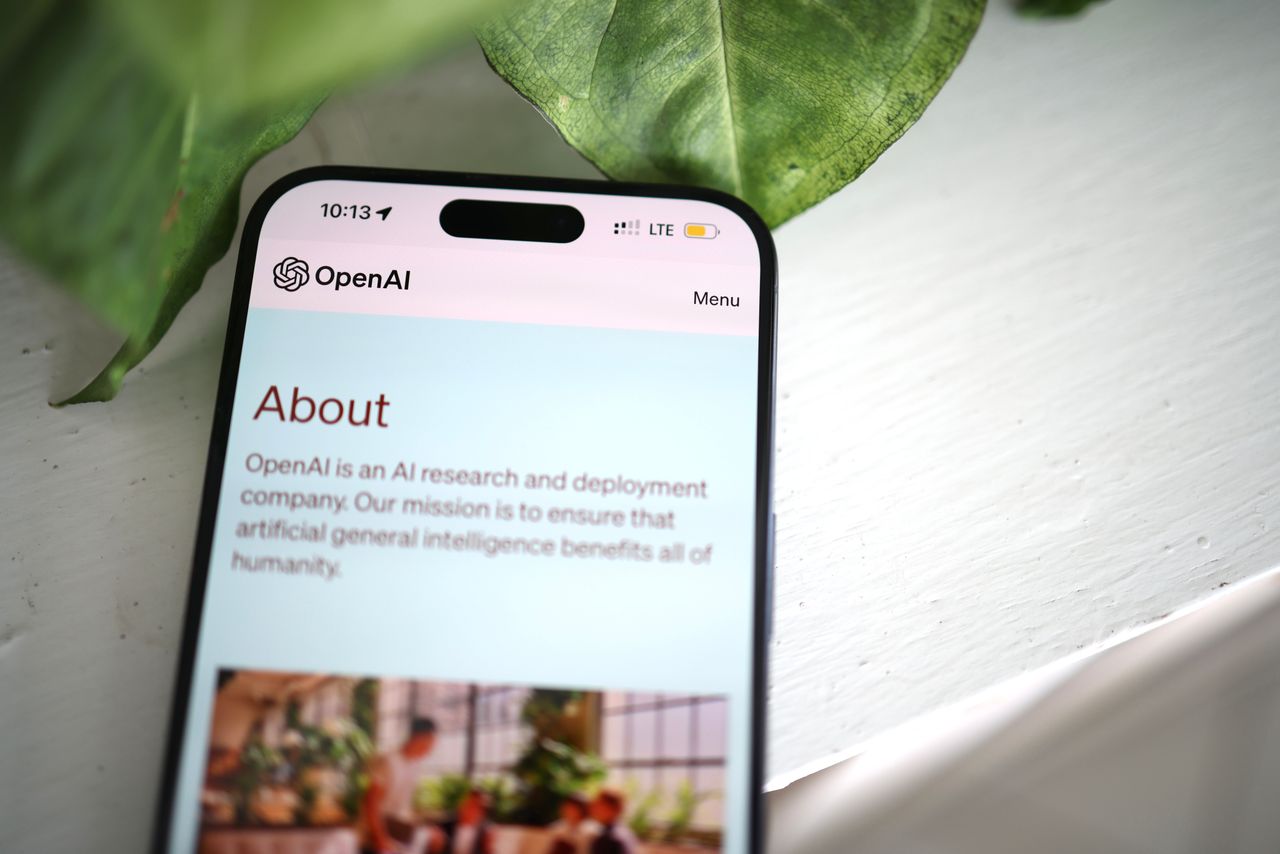 मुखपृष्ठ Close-up shot of a smartphone screen showing the OpenAI website with greenery in the background.